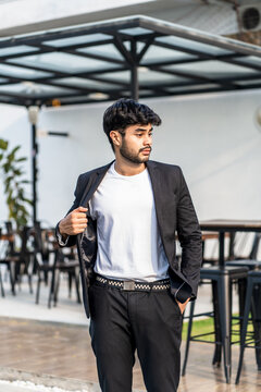 A bearded man doing a pose wearing white shirt with suit as the outer on the outdoor