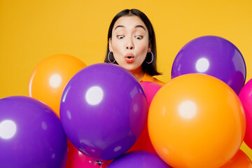 Fototapeta na wymiar Close up excited shocked pop-eyed surprised fun young woman wearing casual clothes celebrating behind bunch of balloons isolated on plain yellow wall background. Birthday 8 14 holiday party concept.