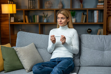 One strip on pregnancy test. Upset woman cannot get pregnant, crying on the couch at home. Unwanted pregnancy, Desperate woman received negative results after IVF.