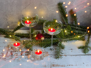 Fototapeta na wymiar Decorative Christmas card. Champagne glasses decorated with candles on Christmas tree branches, with a garland.