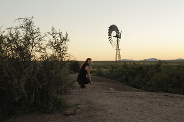 girl walking on a farm road at sunset, windmill