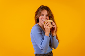 Portrait of cheerful woman eating a sandwich on a yellow background, healthy and vegetarian food