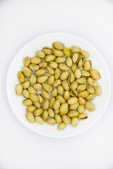 Delicious pistachios on a white plate. Pistachios in a pile on a white plate. Appetizer for beer.