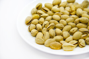 Delicious pistachios on a white plate. Pistachios in a pile on a white plate. Appetizer for beer.