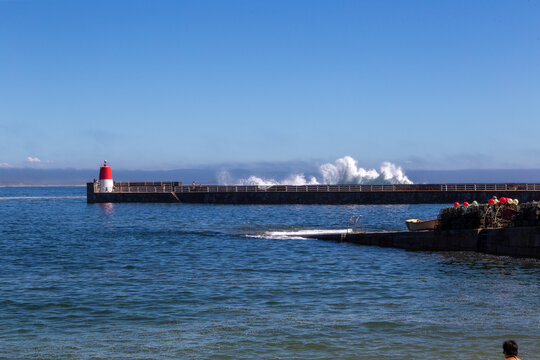Muelle con un peque&ntilde;o faro rojo y una ola rompiendo por encima. Corrubedo, A Coru&ntilde;a, Espa&ntilde;a.