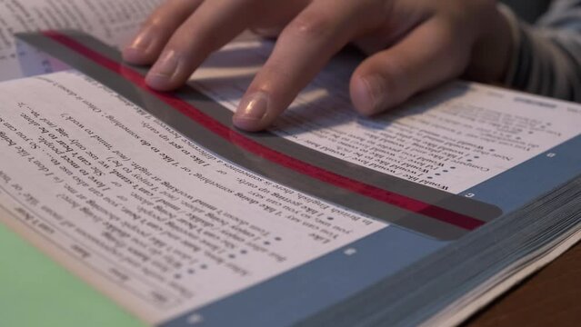 Reading tools for dyslexia. Child doing homework, reading book using colorful ruler overlay strips. Education, learning disability, reading difficulties concept
