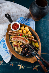 Lunch sausages, stewed cabbage with cranberries, potatoes, tomatoes and sauce in a cast iron skillet.