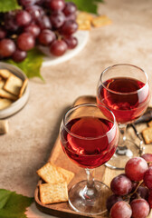 Two glasses of red wine, a bunch of red grapes, crackers and corkscrew on a wooden tray on beige textured background. Celebration party for two concept