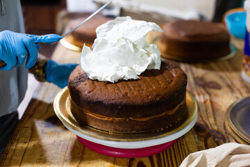 Young woman chef decorating cake with cream. Small baking business.