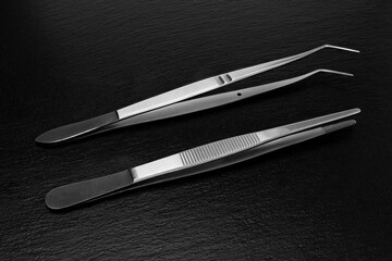 Two Medical surgical tweezers on a black slate background, close-up.