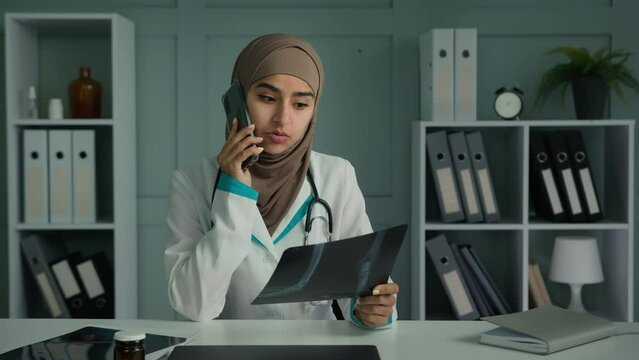 Young doctor arabian turkish woman in hijab islam religion female radiologist work in surgical medicine talking mobile phone examine x-ray broken bones image share with patient bad tomography result 