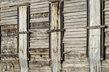 Old wooden siding of a historic structure with its windows covered showing the weathered look of its age.
