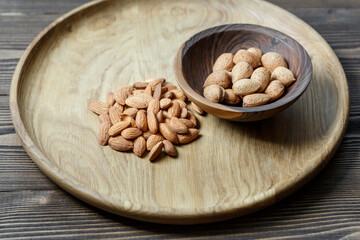 Peeled raw almonds on a wooden plate and almonds in a shell in a wooden bowl on a wooden background.