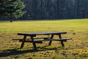 Fototapeta premium Old picnic tables in a park in the late fall with the sun casting shadows.
