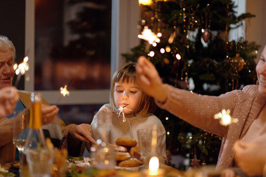 Portrait of little girl sitting at Christmas table trying to extinguish sparkler