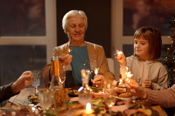 Horizontal portrait of senior woman and little girl burning sparklers at Xmas party