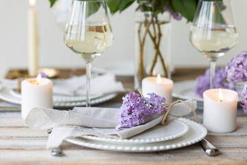 Beautiful table decor for a wedding dinner with a spring blooming lilac flowers. Celebration of a special event. Fancy white plates, wineglasses, candles. Countryside style
