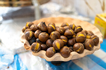 Plate with roasted cracked chestnuts on an old table in the market for sale
