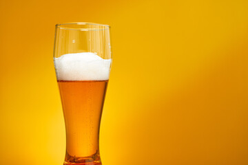 Freshly poured beer in a glass on a yellow background
