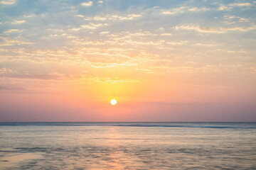 Beautiful sunrise at sea. Dawn on the Red Sea. The sun is reflected in the sea. Light clouds in the blue dawn sky. Tropical sunrise.Flattened sea in long exposure