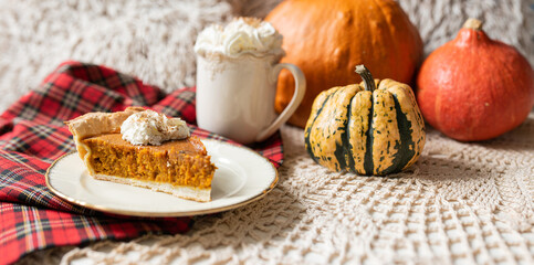 Pumpkin pie topped with whipped cream with coffee or chocolate and pumpkin in backround, rustic set with red tartan accents