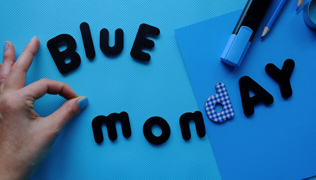 Chica haciendo el s&iacute;mbolo de okey en un fondo azul con letras de Blue monday con material de papeler&iacute;a azul. Blue monday alegre