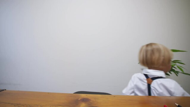 5 years old caucasian boy dressed smart in white shirt and black tie bow takes away a big black notebok with banknotes in it. Little accountant hides banknotes in the notebook