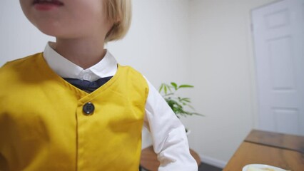 Close portrait of a caucasian boy in bright waistcoat talking to someone behind the camera. 5 years old boy with fair hair has a conversation with someone