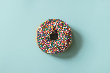 Chocolate Donut with Rainbow Sprinkles on Light Blue Background