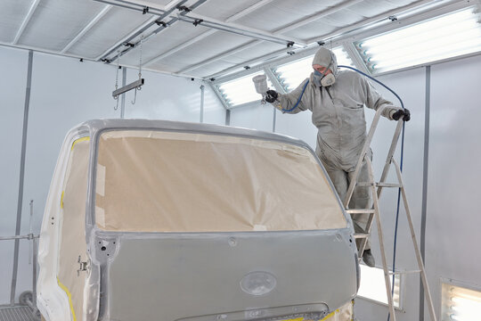 Unrecognisable man wearing work clothes and respirator painting truck using spray gun