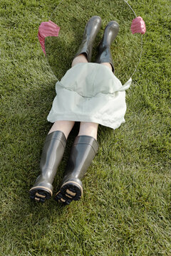 Conceptual photo of unrecognizable woman sitting on green lawn and holding mirror reflecting her legs in gum boots 