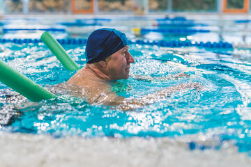 Side view of older adult man swimming with a pool noodle . High quality photo - Powered by Adobe