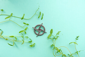 ireland Brigid's cross amulet and leaves close up on abstract green background. Brigid's cross - symbol of Imbolc sabbat. Wiccan tradition for blessed, protection. spring and winter pagan ritual. - obrazy, fototapety, plakaty