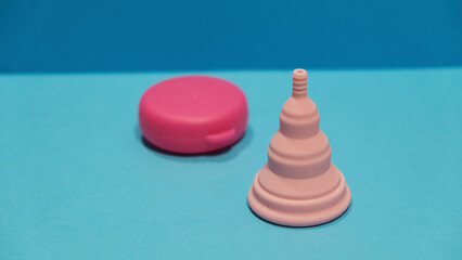 Copa menstrual rosa plegable con su estuche rosa en un fondo azul 