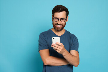 Happy man looking at smartphone on light blue background