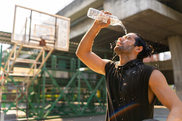Caucasian sportsman basketball player drinking and pouring water from a bottle on his face after do...