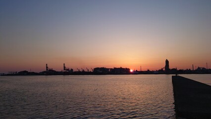 Fototapeta na wymiar 工場をバックに沈む太陽と赤く染まる空と海