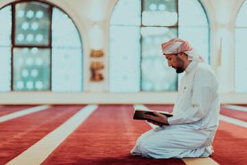 Fototapeta premium A Muslim reads the holy Islamic book Quraqn in a modern grand mosque during the Muslim holy month of Ranazan