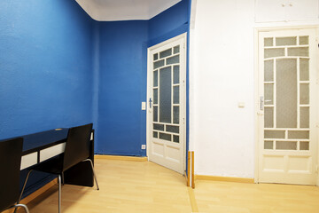 A room with old solid wood doors with translucent windows, blue and white walls and a black desk with white drawers