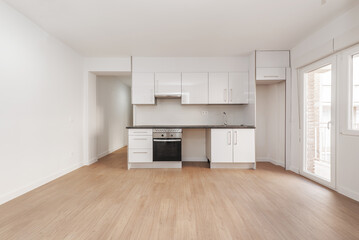 Newly furnished kitchen in an empty apartment with wooden floors, exit to a terrace with a glass door and waiting for the arrival of the refrigerator and washing machine