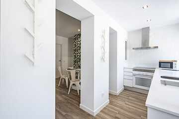 Fototapeta na wymiar Kitchen with white wooden furniture, with a worktop in the same color and access to a living room with a round table