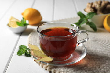 Cup of delicious ginger tea and ingredients on white wooden table