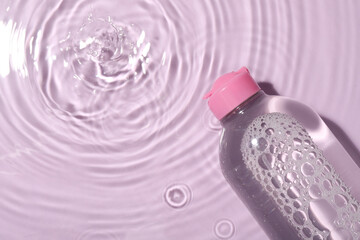 Wet bottle of micellar water on violet background, top view. Space for text