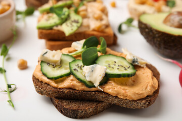 Delicious sandwich with hummus and ingredients on white table, closeup