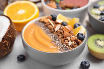 Bowl of delicious fruit smoothie with fresh orange slices, blueberries and granola on white table, closeup