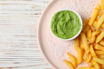 Plate with french fries and avocado dip on white wooden table, top view. Space for text