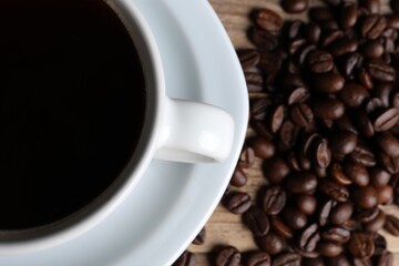 Cup of hot aromatic coffee and roasted beans on wooden table, top view. Space for text