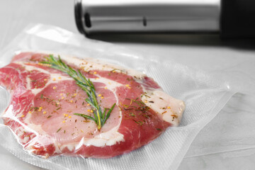 Sealer for vacuum packing with plastic bag of meat on light grey table, closeup