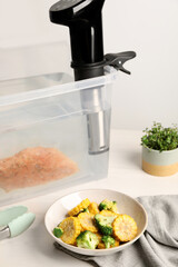 Thermal immersion circulator and vacuum packed meat in box on white wooden table. Sous vide cooking