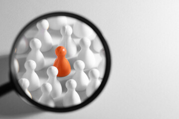 Magnifying glass over pawns on white background, space for text. Recruiter searching employee